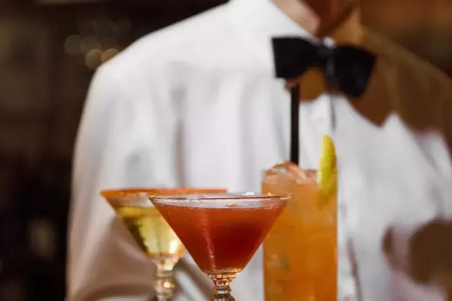 A server wearing a bowtie presents a tray of cocktails at Absinthe Restaurant in San Francisco.